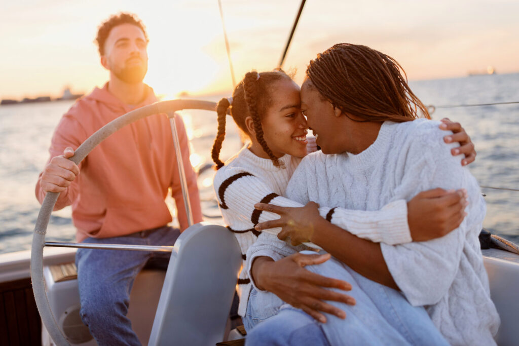 Family Cruisers | Top Yachts & Sailboats for Comfort | YATCO Father sailing one of the family cruisers while mother and daughter embrace and enjoy the view.