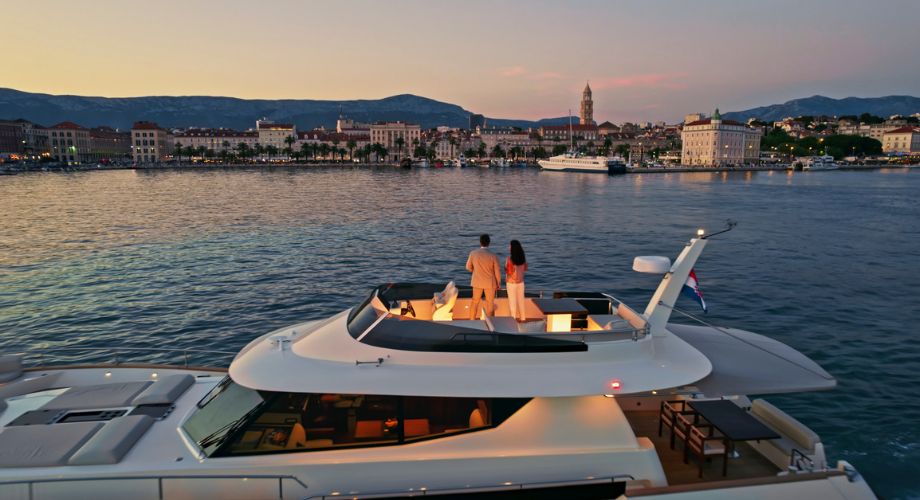 Yacht Ownership | YATCO A couple standing on the top deck of a luxury yachts that's sailing in the ocean during sunset.